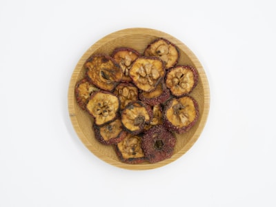 A wooden plate with dried fruit slices, featuring visible seeds and a slightly wrinkled texture. The fruit slices are arranged in a circular pattern on the plate.