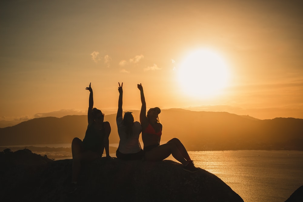 three women sitting on a rock with their arms in the air