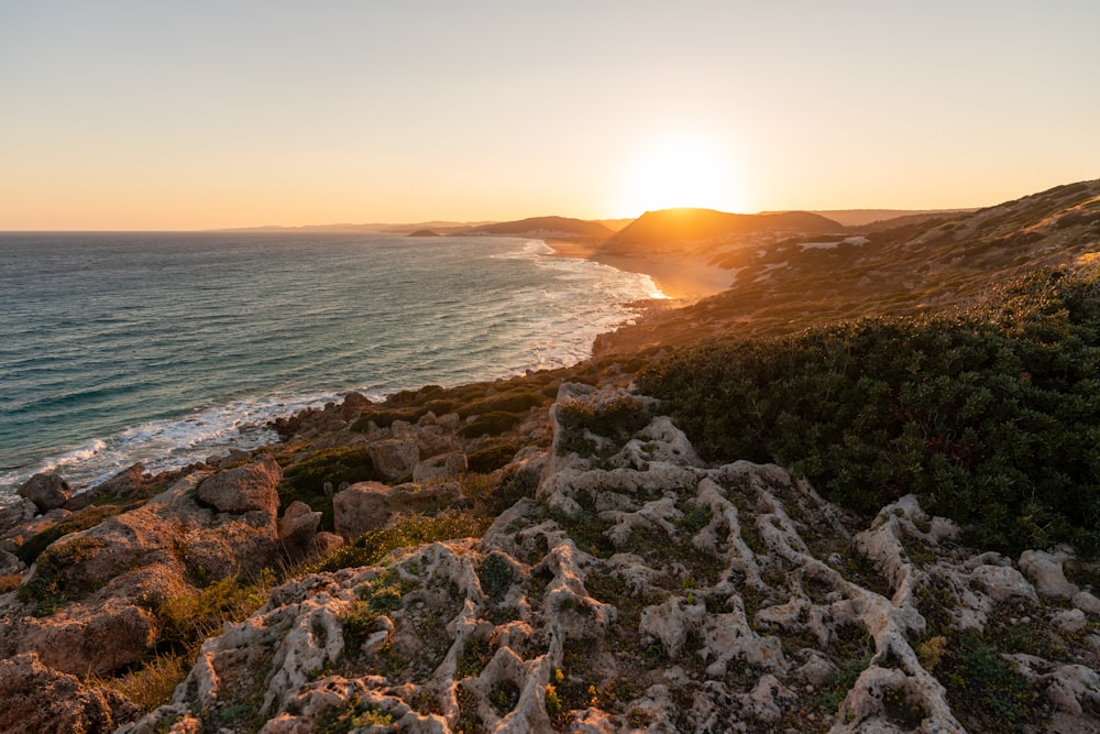 the sun is setting over the ocean on a rocky shore