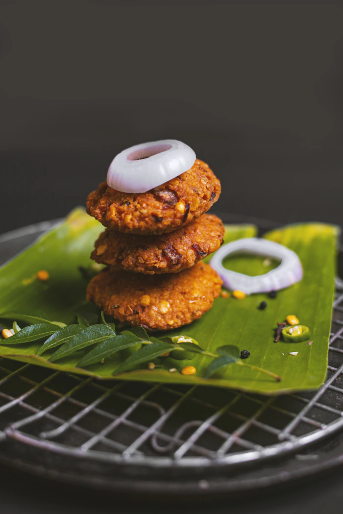 Masala vada stacked on a banana leaf with onion rings