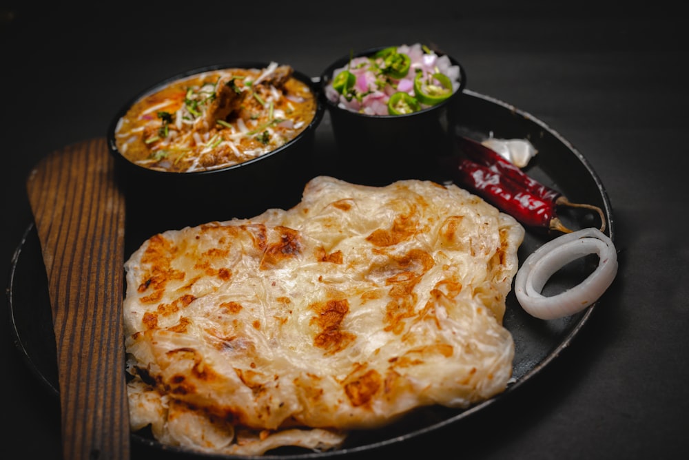 a black plate topped with food next to a bowl of salad