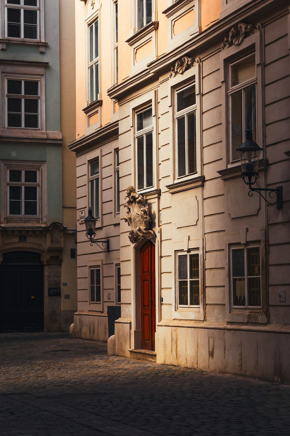 an old building with a red door in the middle of a cobblestone street