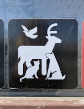 A graphic symbol illustrates various animals in a simplistic, minimalist style. The design features a large deer in the center, a cat at its feet, a seated dog to the side, and a bird flying above.
