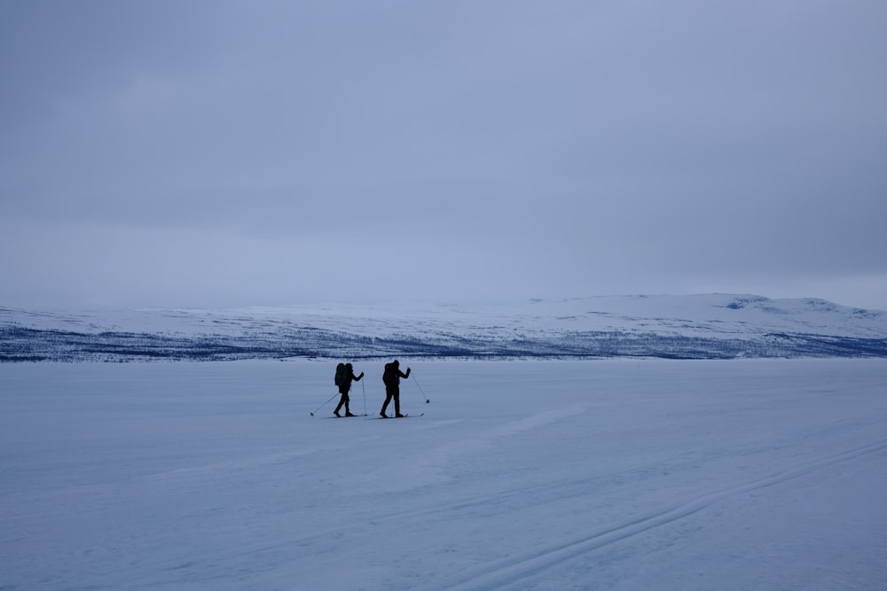 a couple of people walking across a snow covered field