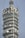 A close-up view of a tall telecommunications tower equipped with numerous satellite dishes and antennas arranged in circular tiers. The structure is metallic and industrial in design, showing intricate technical components.
