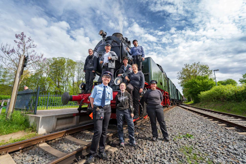Young railway employees training together on a vibrant football field under clear skies.