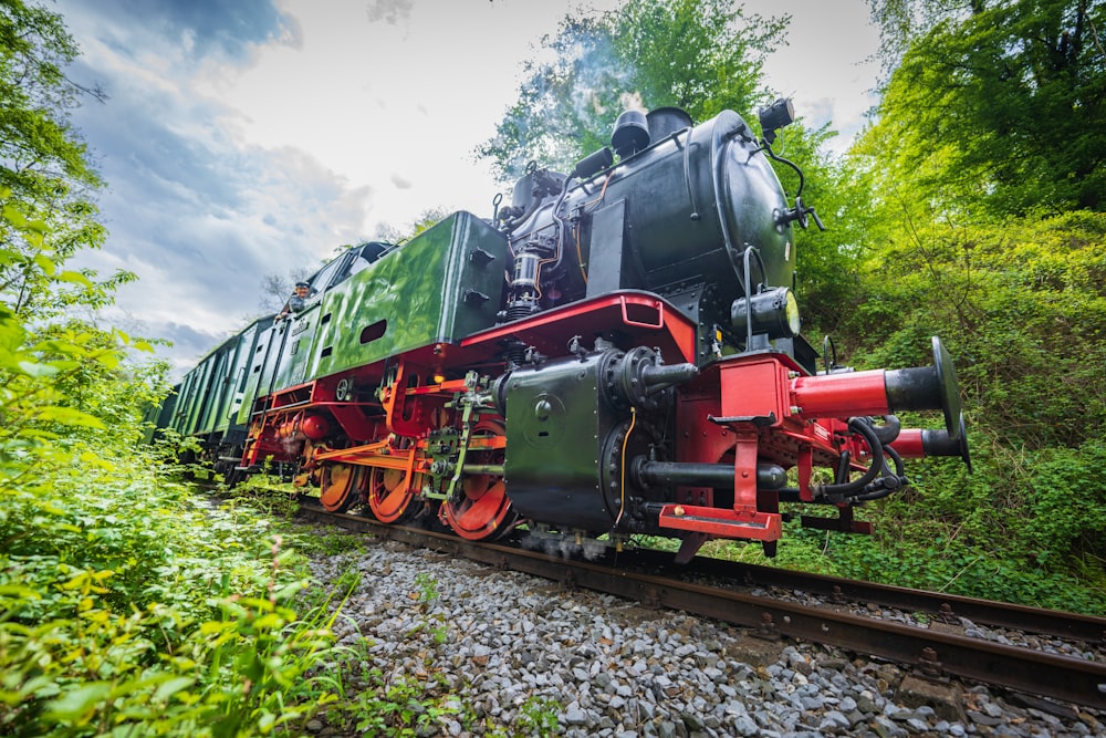 a green and red train traveling through a lush green forest