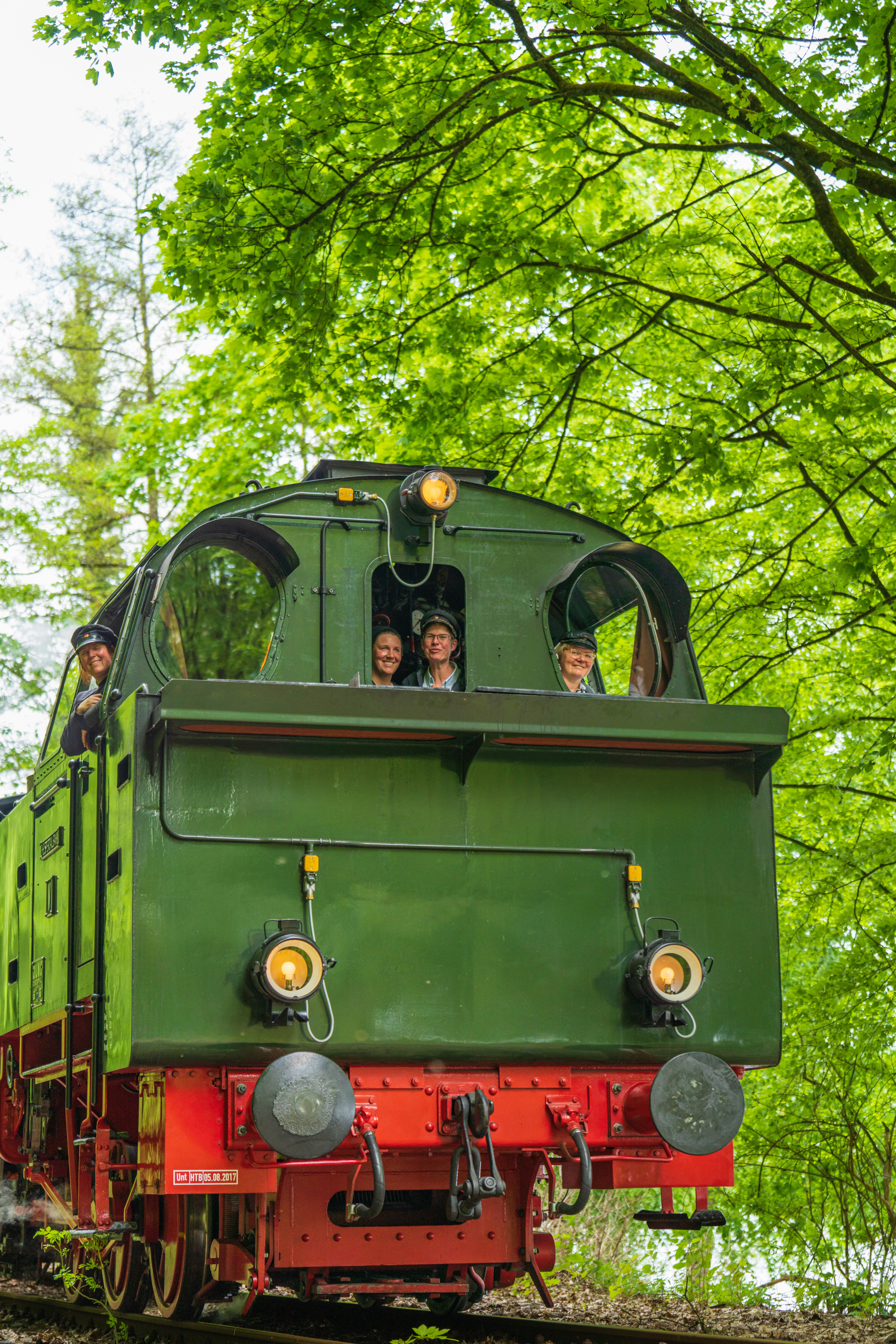 a green train traveling through a lush green forest