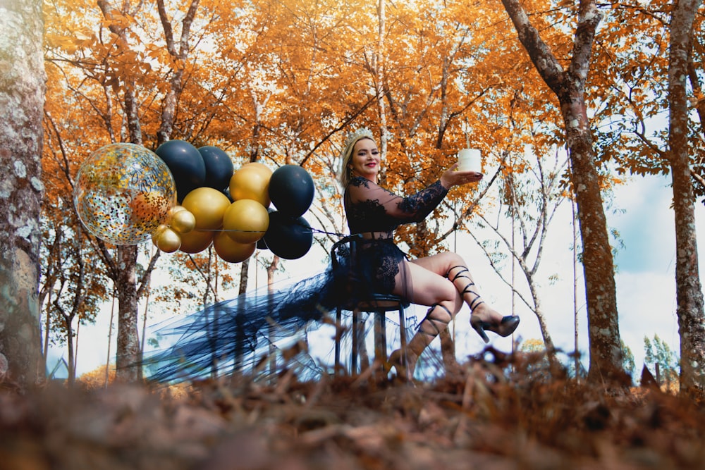 a woman sitting on a chair in a forest with balloons