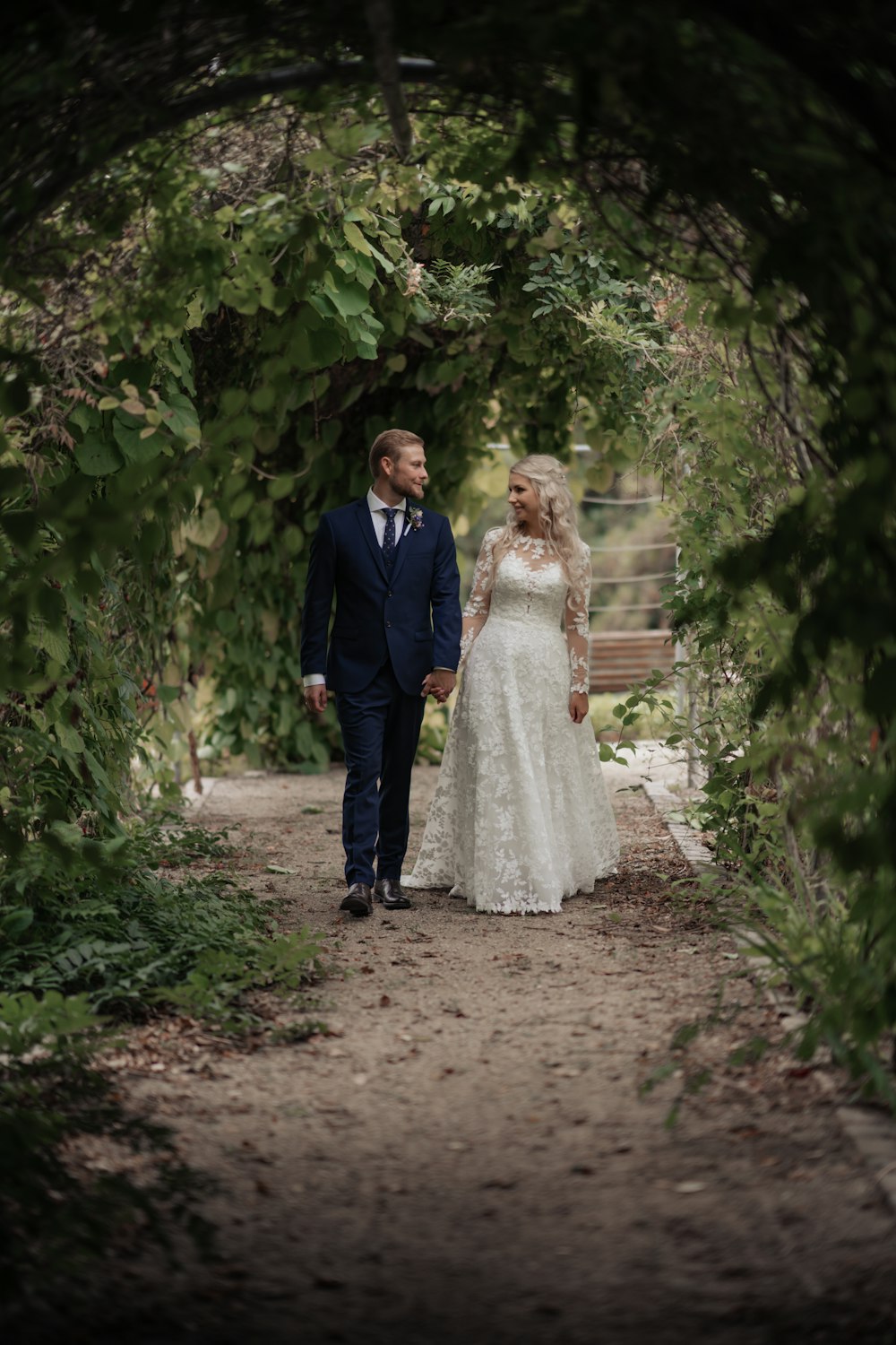 a bride and groom walking through a tunnel of trees