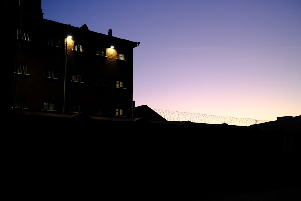 a silhouette of a building at dusk with lights on