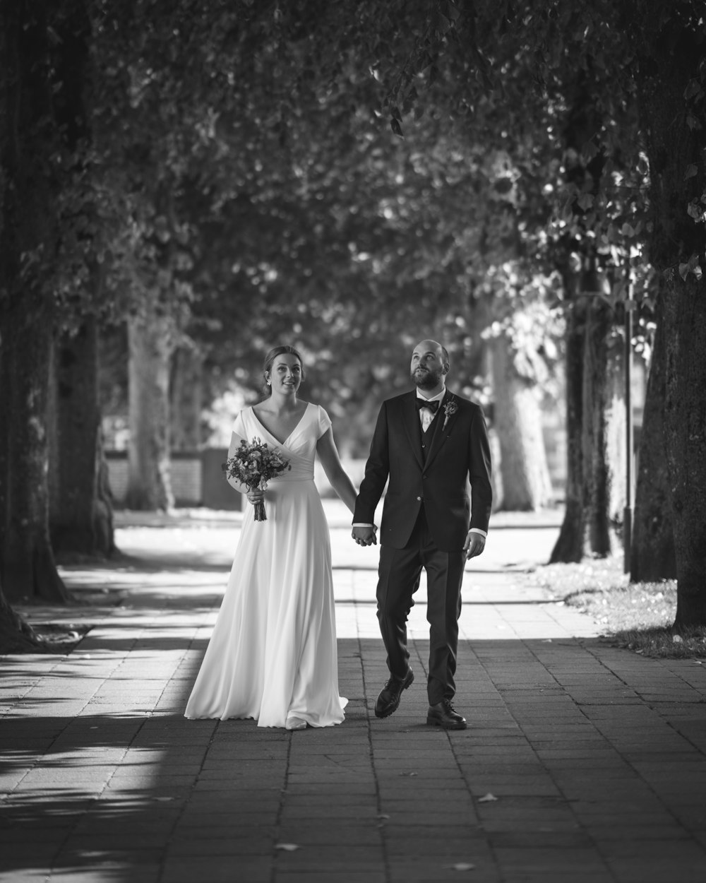 a bride and groom walking down a sidewalk holding hands