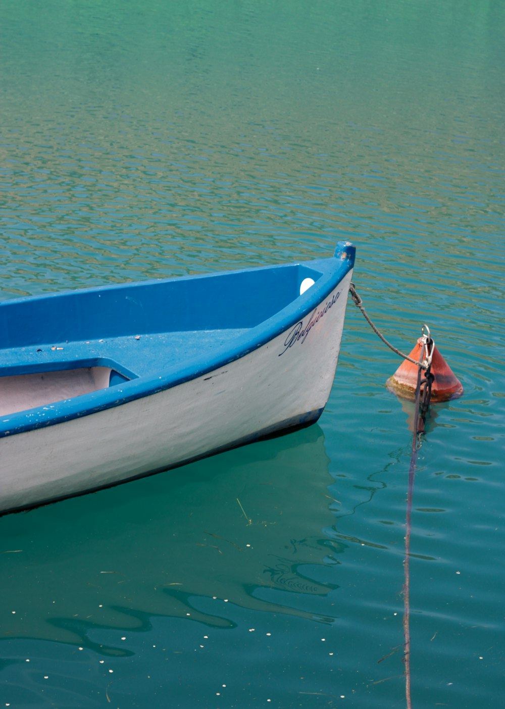 a blue and white boat tied to a pole in the water
