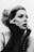A black and white portrait of a person with styled hair and dramatic makeup, including winged eyeliner and bold lipstick. The individual wears long, lace, fingerless gloves and poses with hands framing their face, exuding a sense of elegance and contemplation.