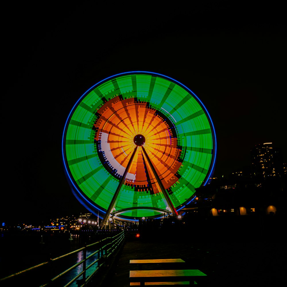 a ferris wheel lit up at night with buildings in the background
