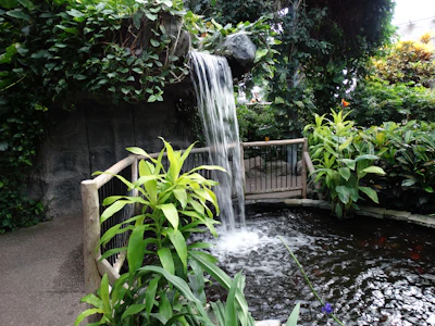 A serene handcrafted ornamental waterfall surrounded by lush greenery and natural stones.