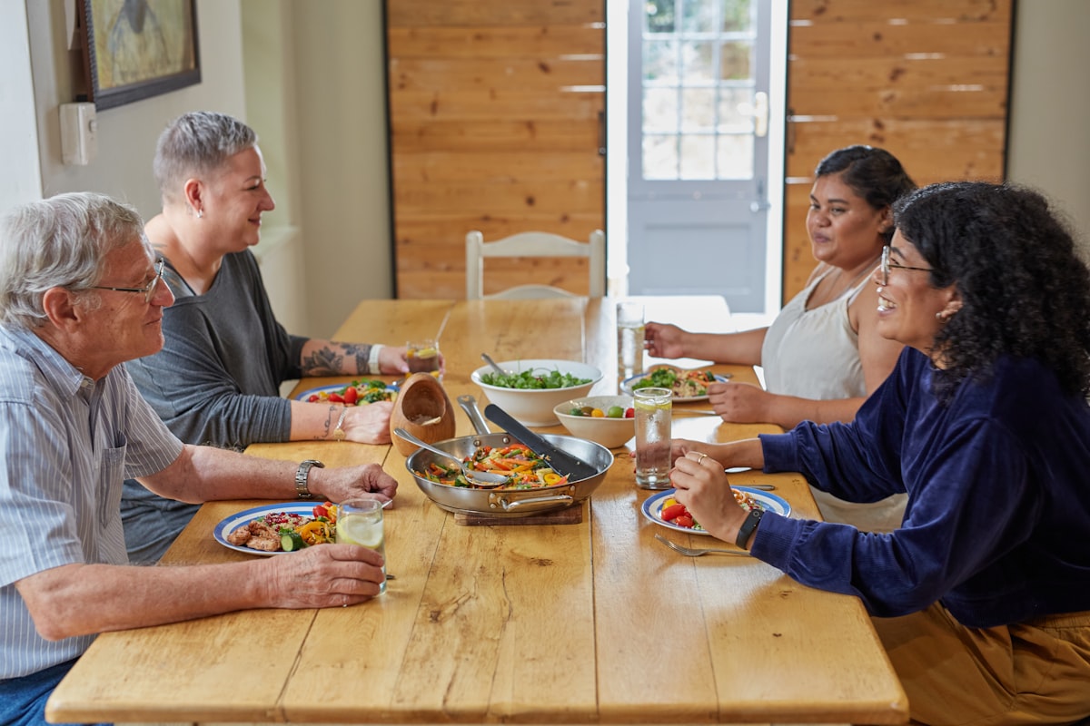 A caregiver and family sharing a meal around a wooden table