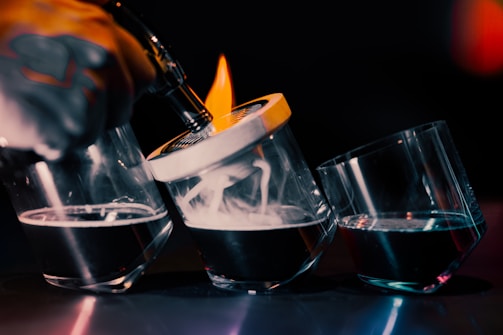 A close-up of the saturix electric whiskey smoker glowing amber inside a smoky, dark bar setting with golden rings of smoke swirling around.