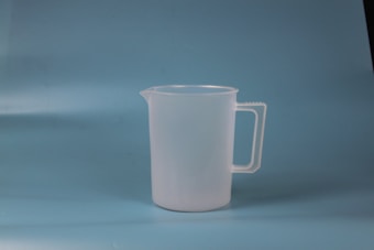 A translucent plastic measuring jug with a handle, placed against a plain blue background.