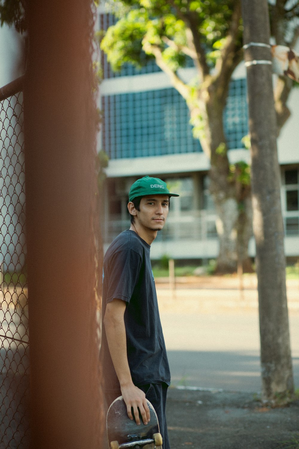 a young man holding a skateboard next to a fence