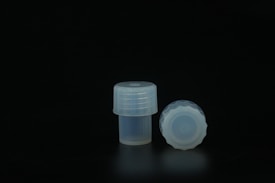Two translucent plastic caps are placed against a dark background. One cap is upright, displaying its cylindrical shape with textured sides, while the other lays on its side, revealing grooved patterns along the top edge.