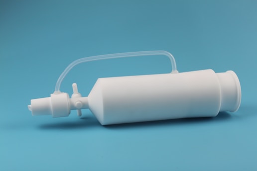 A white plastic bottle with a narrow nozzle and an attached flexible tube is set against a solid cyan background.