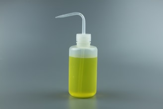 A clear plastic squeeze bottle filled with yellow liquid, featuring a bent spout for easy dispensing, against a plain gray background.
