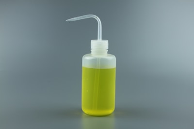 A clear plastic squeeze bottle filled with yellow liquid, featuring a bent spout for easy dispensing, against a plain gray background.