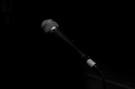 A microphone is prominently displayed against a dark background, angled slightly upwards, suggesting a setting for performance or recording.