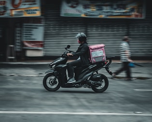 Delivery person on a scooter with pink and black branded bags ready to deliver laundry.