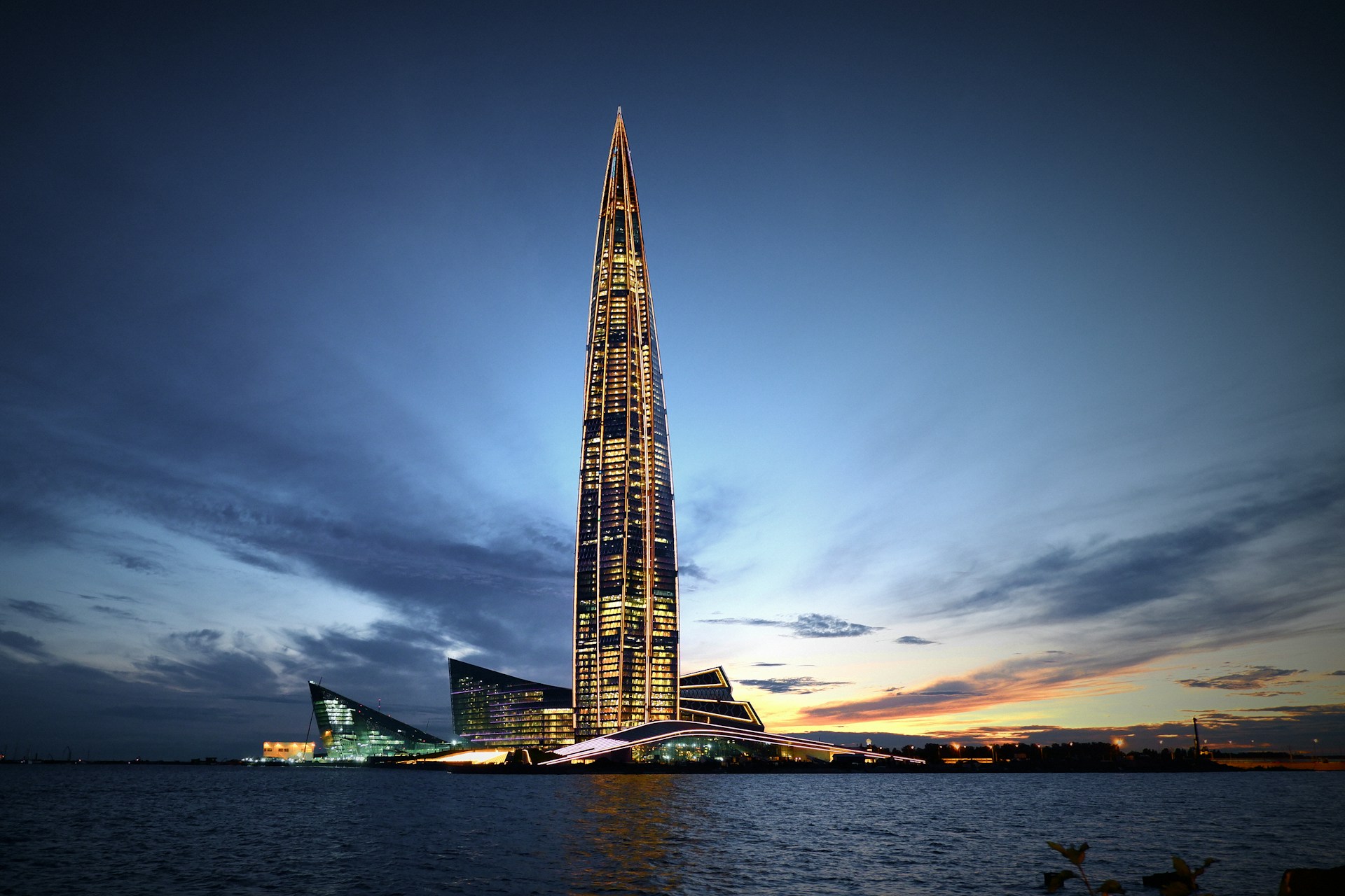 A sleek, towering skyscraper with glowing blue accents piercing a twilight cityscape, embodying futuristic urban elegance.