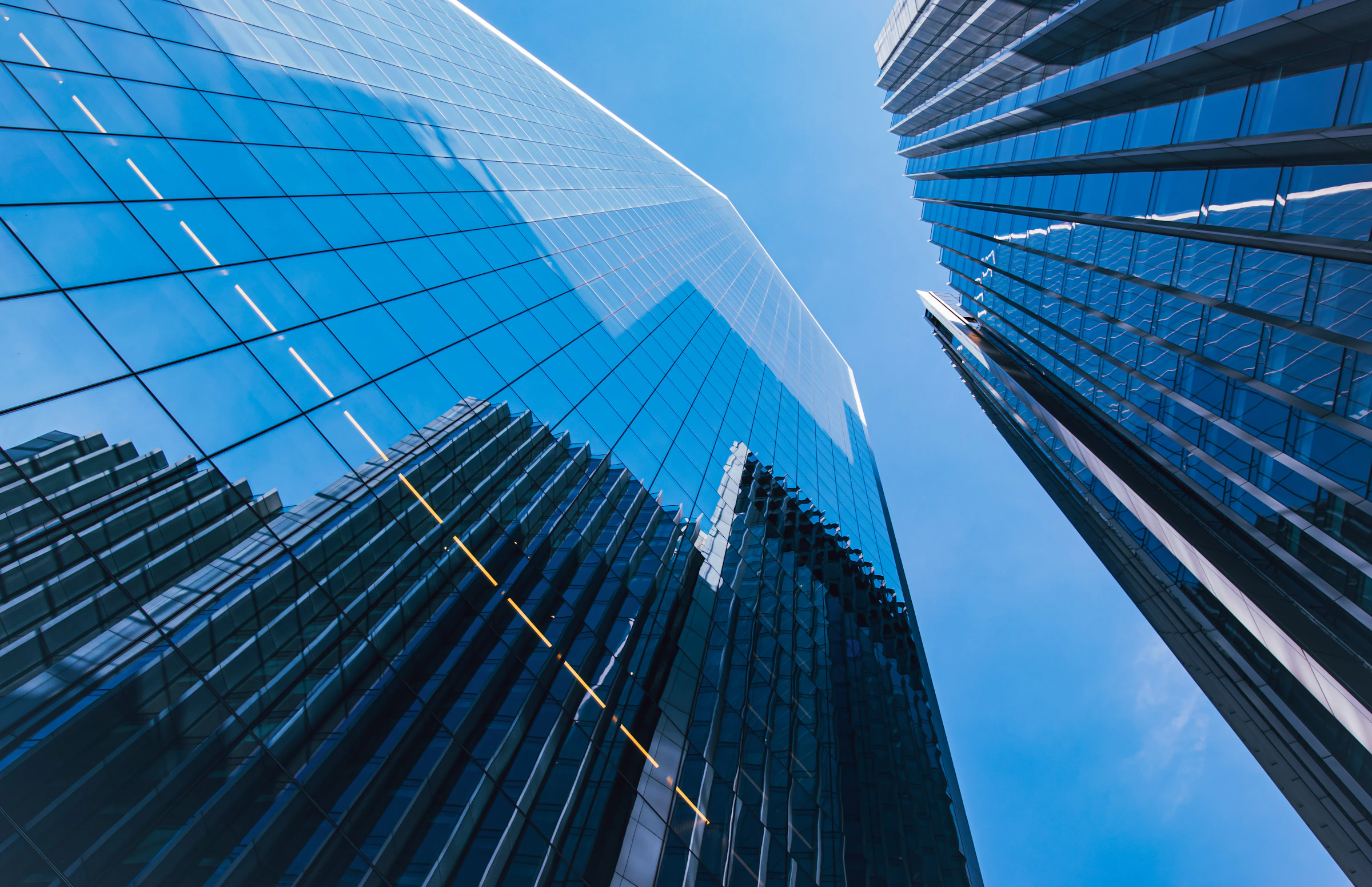 Blue glass towers reflecting one another, seen from the street