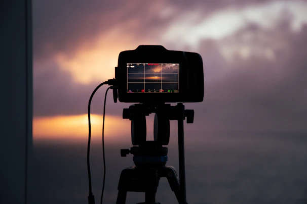 A photographer adjusting a tripod-mounted camera against a sunset backdrop.