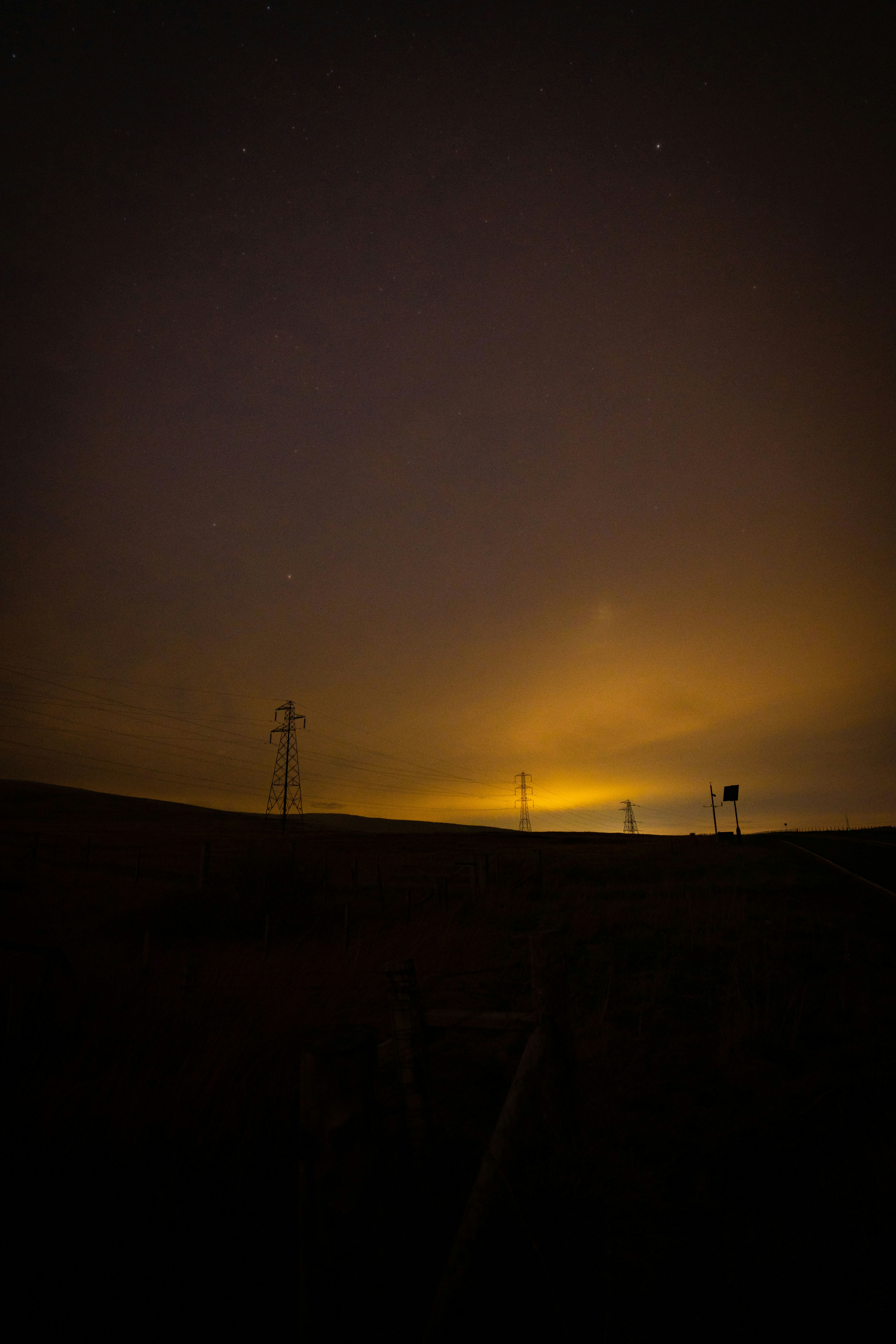 High-voltage transmission towers at golden hour, dramatic sky, steel lattice pylons, warm amber atmospheric lighting