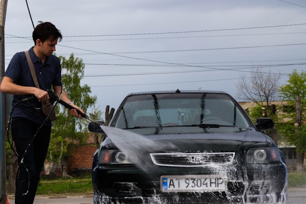 A professional washing a car outdoors with cleaning tools and water spray.