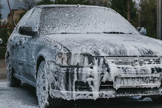 A sparkling clean car being gently washed with rich, foamy soap under bright sunlight.
