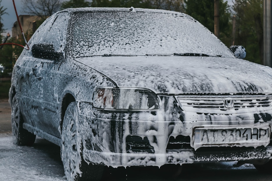 A sparkling clean car being gently washed with rich, foamy soap under bright sunlight.