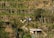 Three individuals are standing on terraced farmland with stone walls and vertical wooden supports for plants. The landscape is lush with greenery, scattered trees, and a small shed.
