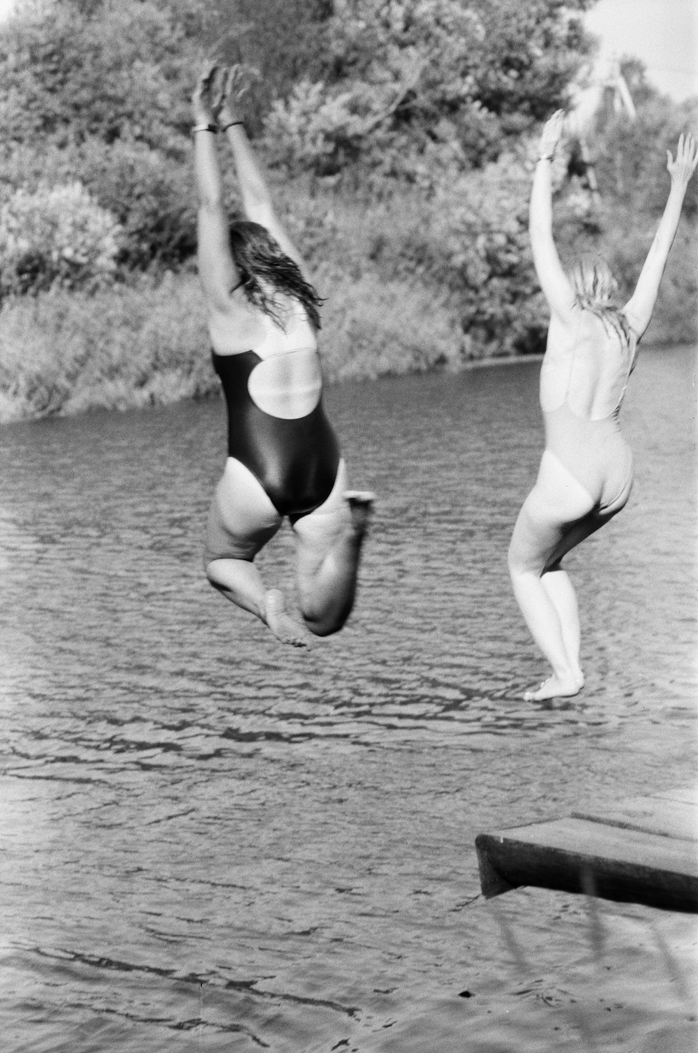 two women jumping off a dock into a body of water