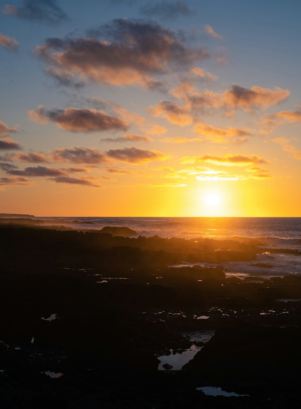 the sun is setting over the ocean on a cloudy day