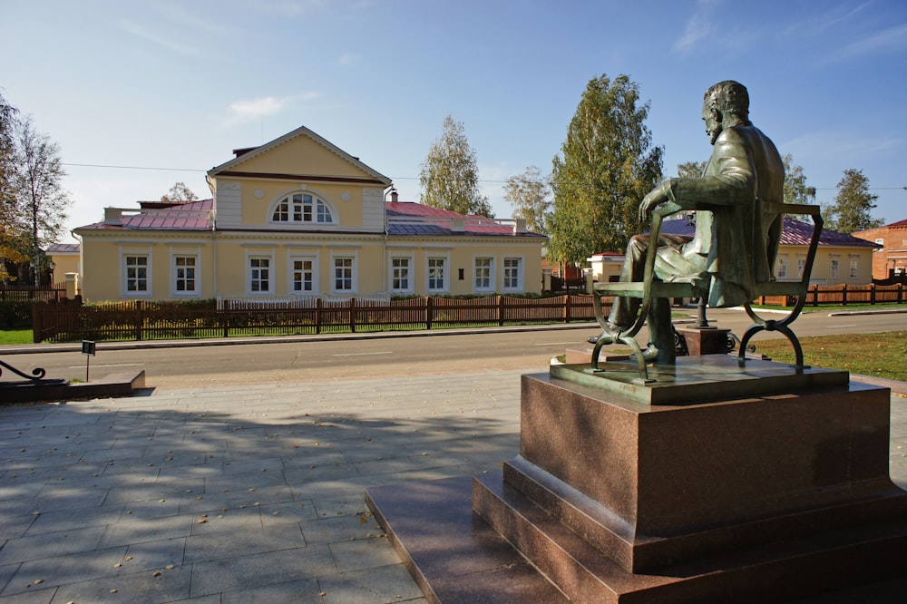 a statue of a man sitting on a chair in front of a building