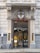 The entrance of a building with ornate architectural features, including decorative columns and a shield emblem above the door. The signage reads 'Church of Scientology London,' and there are glass doors allowing a glimpse of the interior. A bicycle is parked outside, and there are signs related to building access.