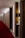 A hotel corridor with a modern design features a long red carpet and minimalist wooden panels. The lighting is soft, casting a warm glow along the hallway. Room numbers are displayed on the wood panels.