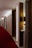 A hotel corridor with a modern design features a long red carpet and minimalist wooden panels. The lighting is soft, casting a warm glow along the hallway. Room numbers are displayed on the wood panels.