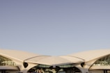 A modern building with a futuristic design featuring sweeping curves and large glass windows. The structure is predominantly white and sits under a clear blue sky. The architecture is reminiscent of mid-century modern design with an emphasis on smooth, aerodynamic shapes.