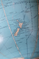 A close-up view of a vintage globe featuring the map of New Zealand, including both the North Island and South Island, with surrounding oceans and labeled cities like Auckland and Wellington.