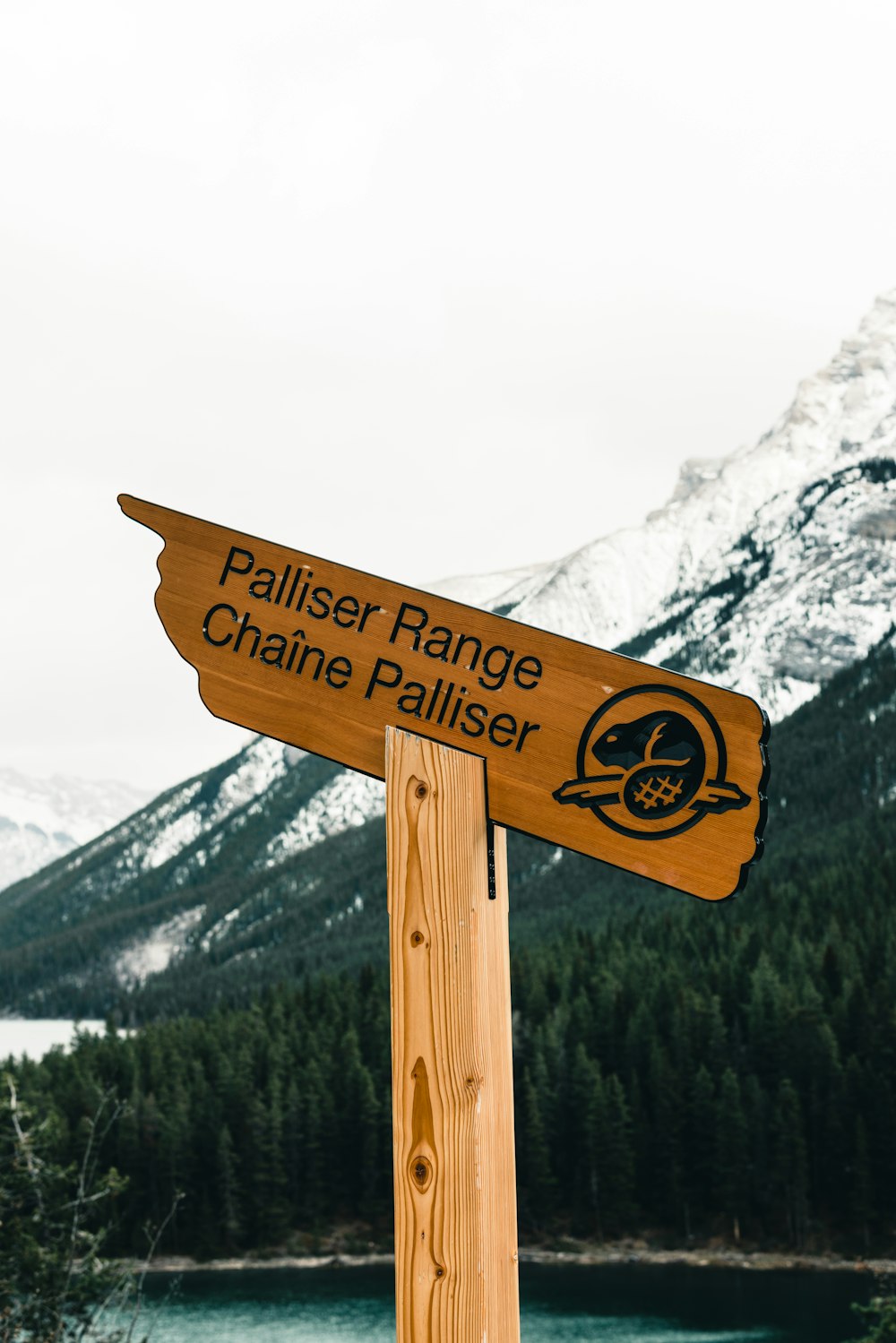 a wooden sign pointing in opposite directions in front of a mountain lake