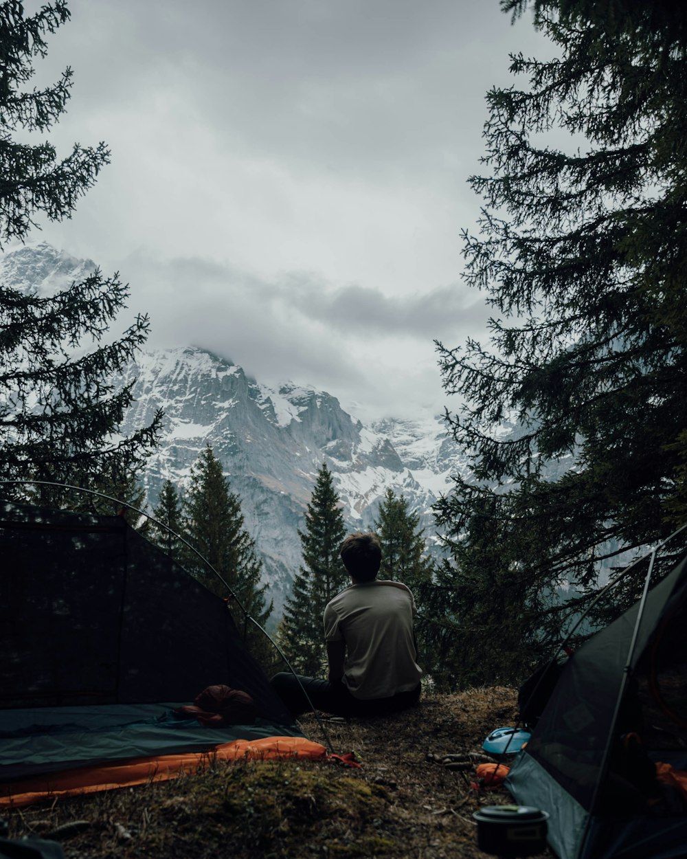 a man sitting next to a tent on top of a forest