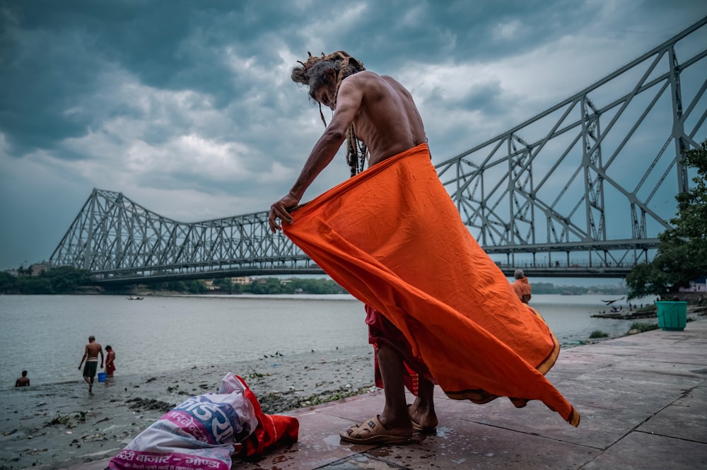 a man with an orange towel on the shore of a river