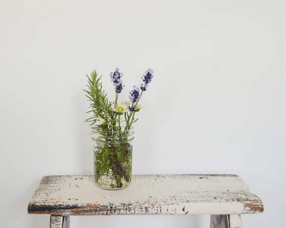 Fresh flowers and leaves artfully scattered around a jar of moisturizer on a rustic table.
